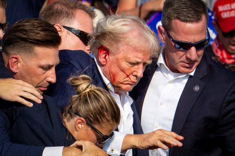 Donald Trump is seen surrounded by secret service agents with blood on his face.