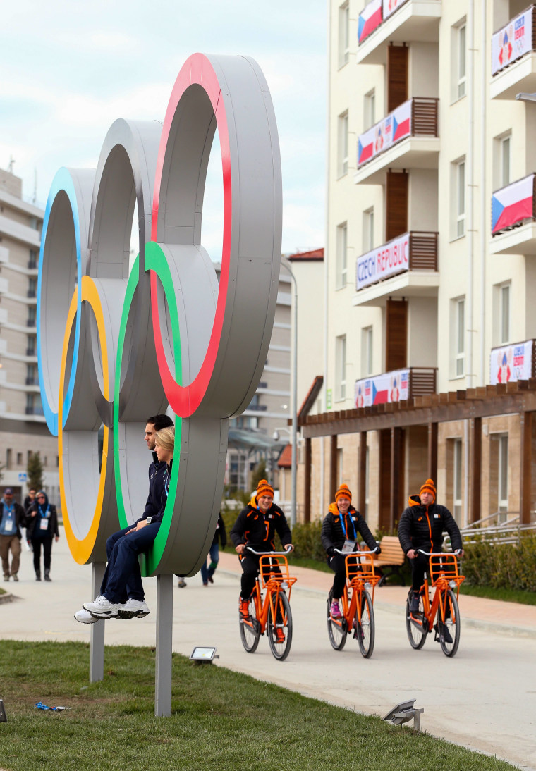 People posing with the Olympic rings and riding bicycles at the Athletes Olympic Village in February 2014 at Sochi, Russia.