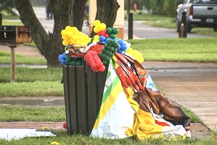 Birthday balloons and other decorations are stuffed into a trash can outdoors