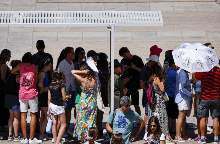 People queue under a shade.