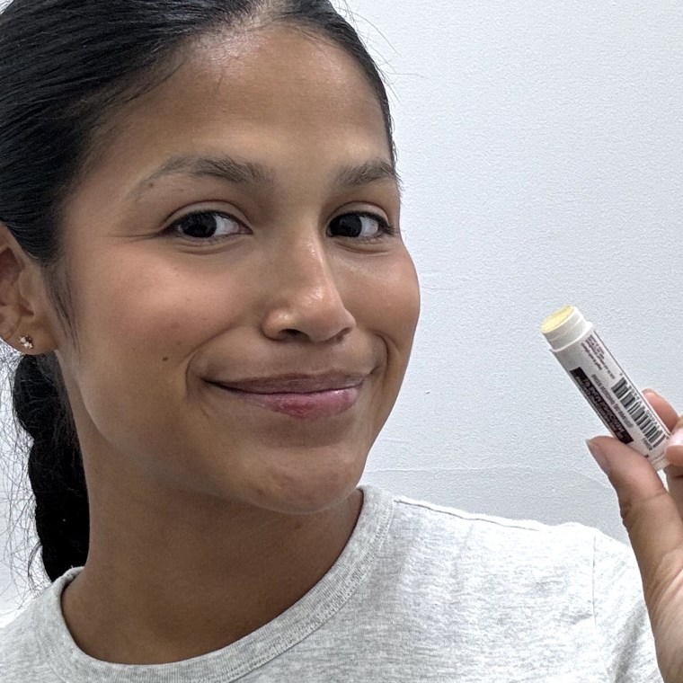 Image of a woman holding lip balm next to her face after applying it.