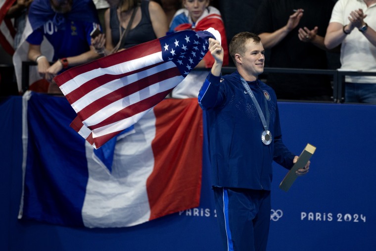 Nic Fink segurando a bandeira americana durante a final dos 100 m peito masculino.