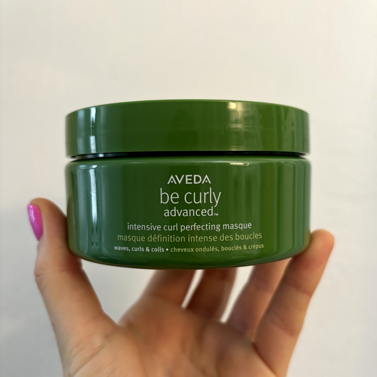 Woman holds the Aveda Be Curly Advanced Intensive Curl Perfecting Masque in her hand.