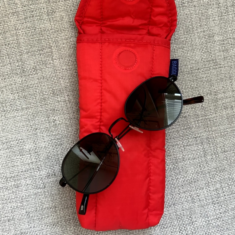 Red Baggu Puffy Glasses Sleeve lays open with black sunglasses on top.