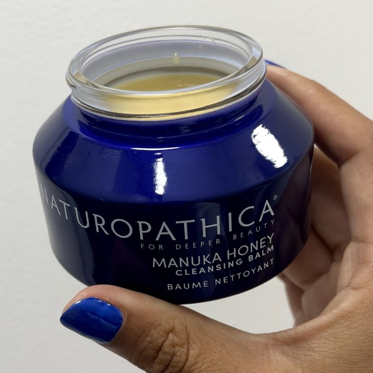 Woman holds uncapped Naturopathica Manuka Honey Cleansing Balm in her hand.