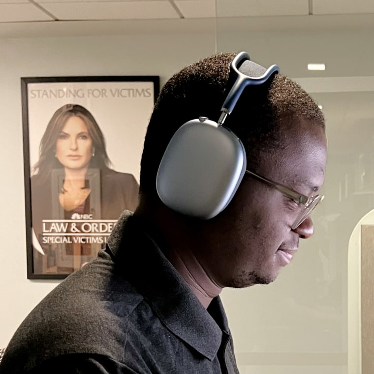 Man wears navy blue Airpods Max headphones while working in the office at his desk.