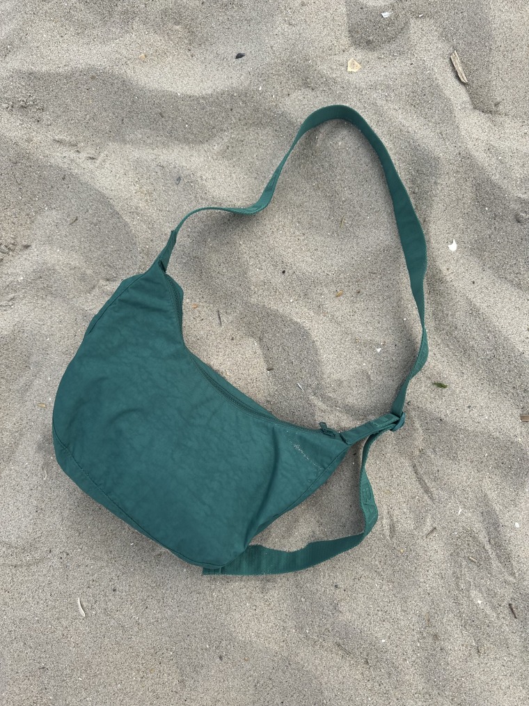 Baggu Cypress crescent bag lays flat on the beach sand.