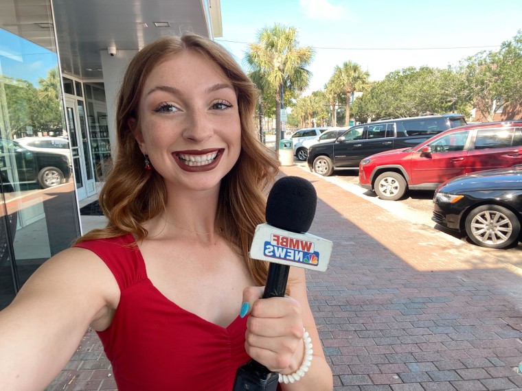 A young reporter in a red top holds a WMBF mic in a selfie photo.