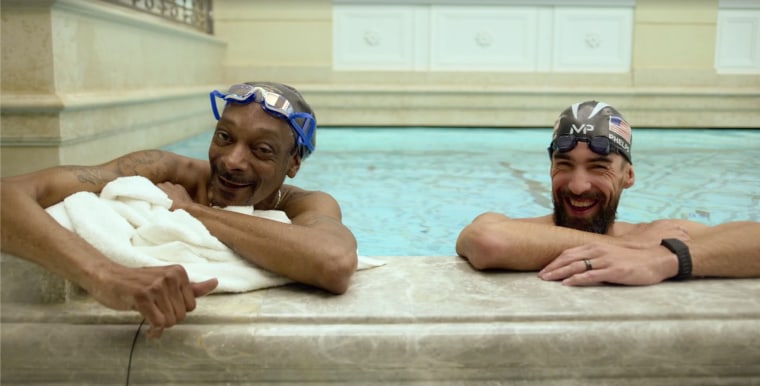 Snoop Dogg and Michael Phelps in swim caps and goggles in a marble hotel pool.