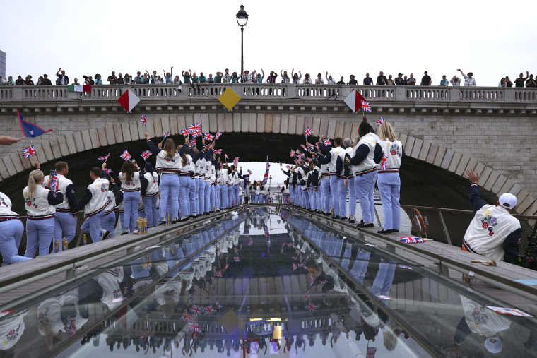 Spectators cheer as Great Britain athletes pass under a bridge along the Seine. 