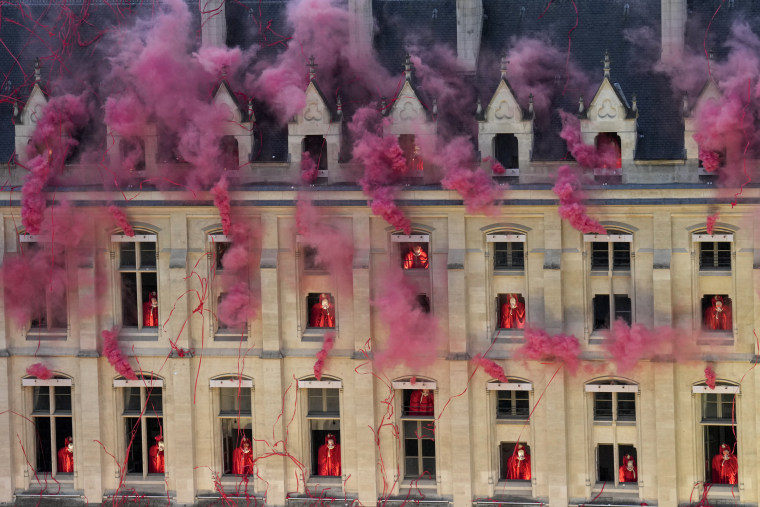 Performers stand in windows as smoke billows.