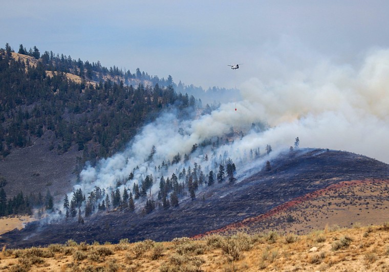 Helicopter crew battles wildfire burning in forest and rangeland.