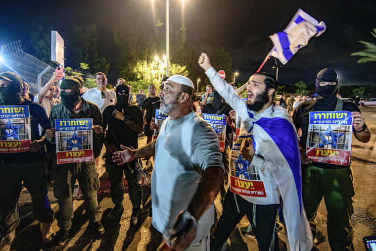 Ativistas de direita torcendo diante de pessoas armadas e mascaradas