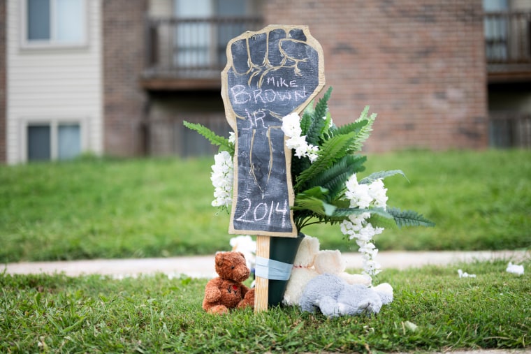 A poster drawing in the shape of a fist that says Mike Brown Jr., 2014, is seen along Canfield Drive in the grass