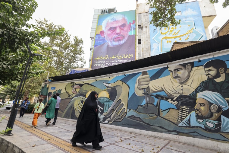 People walk past a billboard showing a portrait of newly appointed Hamas leader Yahya Sinwar in Tehran on August 12, 2024.-ISRAEL-CONFLICT