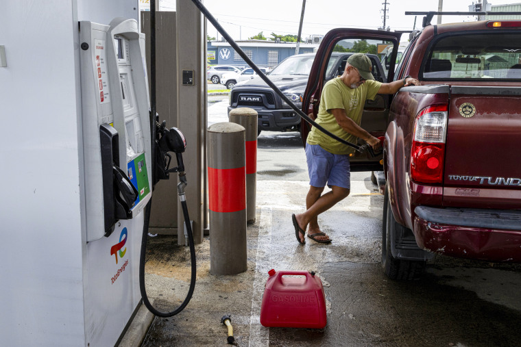 Um homem enche seu carro e coloca mais latas de gasolina.