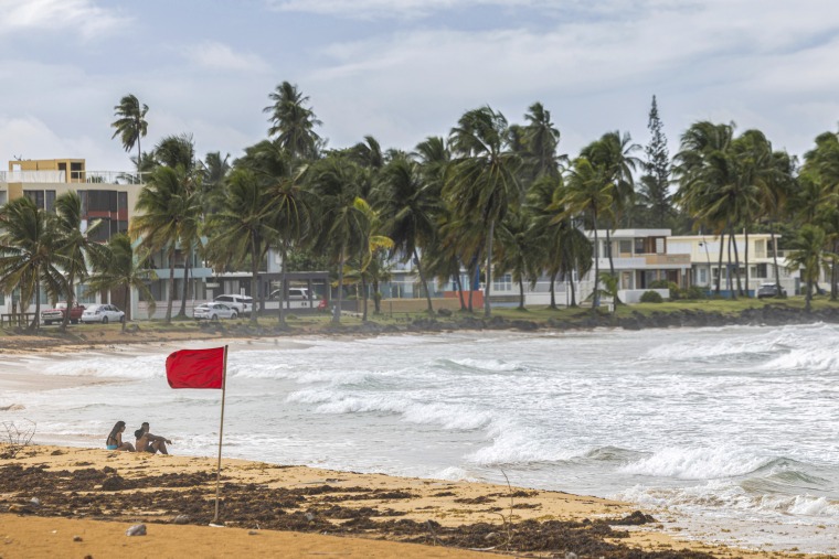 Tourists sit on the beach near a red flag.