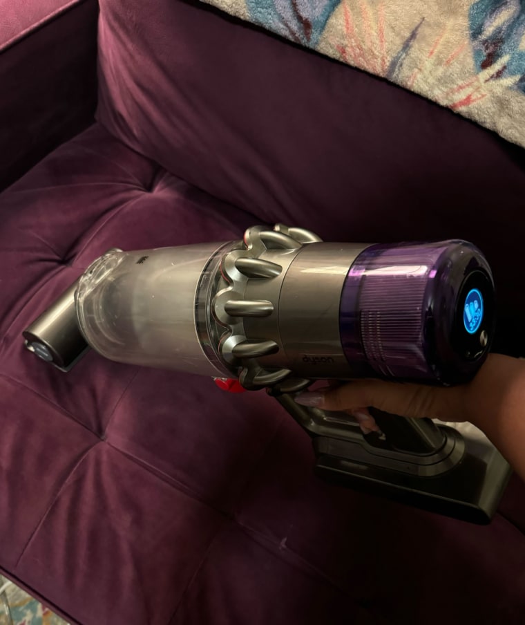 A close up of a Dyson vacuum being used on a purple couch in handheld mode.