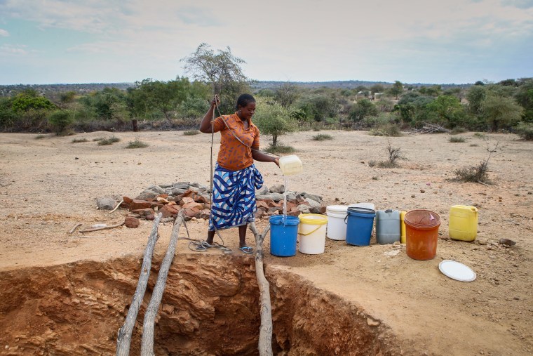 A woman pours a trickle of water into a bucket outside in barren land