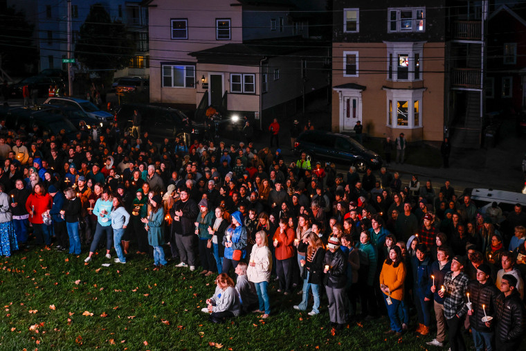 A large group of people on a lawn outside in a residential area hold vigil candles