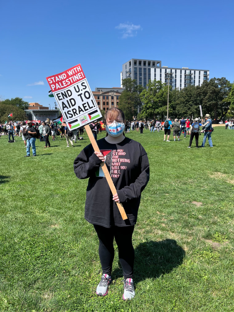 Annie Weiler says outside, holding a sign "Be with Palestine! Stop US aid to Israel!"