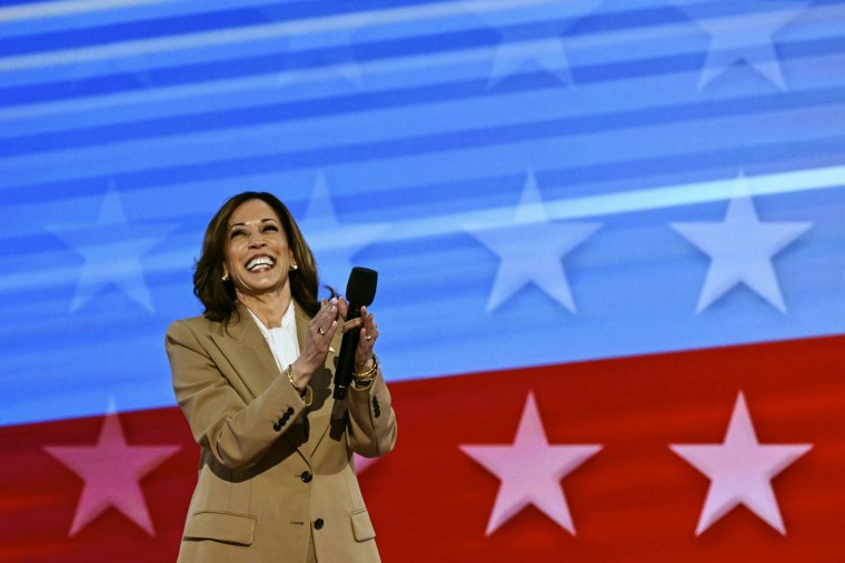 Kamala Harris smiles while holding a microphone on stage