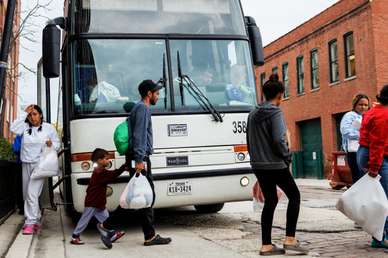 People walk in front of a parked bus to cross the street outside