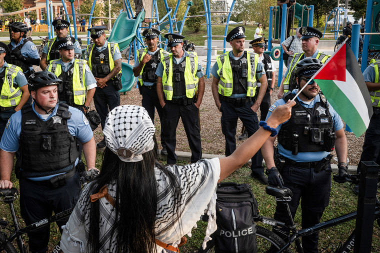 Police stand as demonstrators march with Palestinian flags.