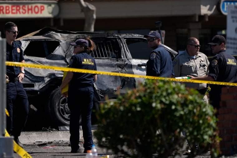 Investigators and police in front of the charred police vehicle