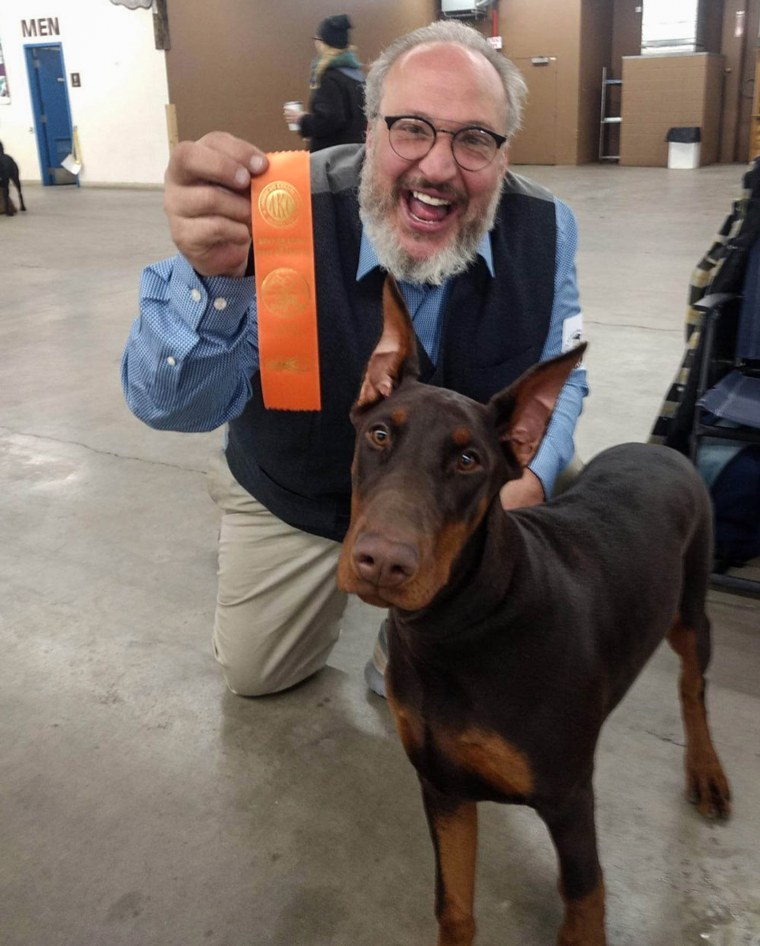 Paul Peavey holds an award while kneeling behind a Doberman