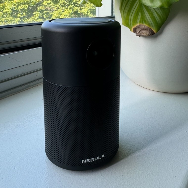 The Anker Nebula Capsule next to a plant on a white ledge.