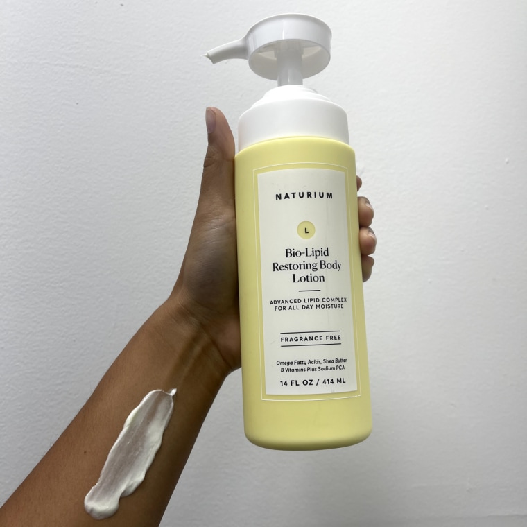 Woman holds a bottle of Naturium Bio-Lipid Restoring Moisturizing Body Lotion with a swatch of the lotion on her arm.