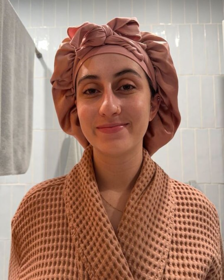 Woman wears a robe and a terracotta-colored Yanibest Satin Bonnet tightly wrapped around her head in her bathroom.