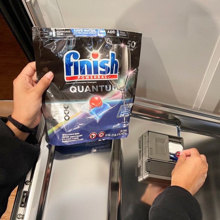 Woman holding bag of Finish Quantum Powerball dishwasher detergent while placing pod in the dishwasher