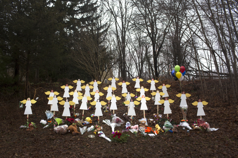 Twenty-seven wooden angel figures along a road with bouquets of flowers surrounding them