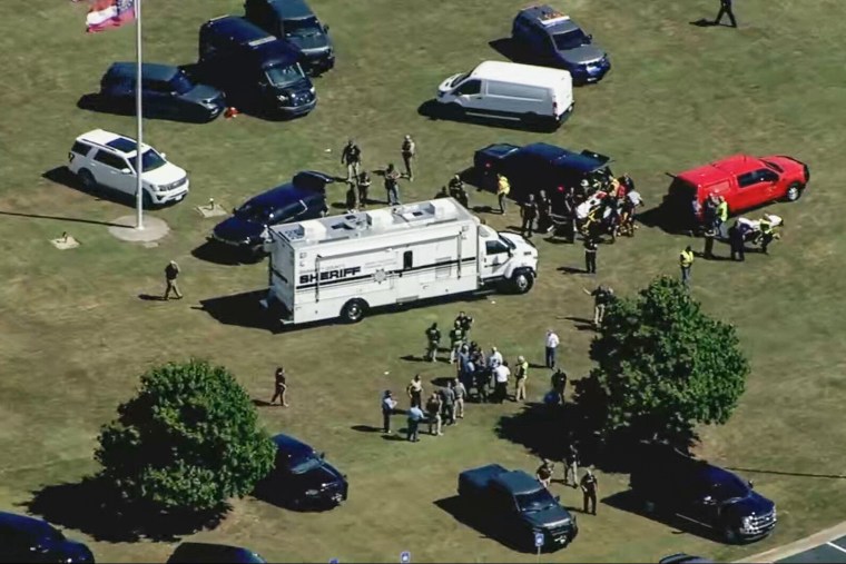 Police officers and officials on the lawn of a high school campus