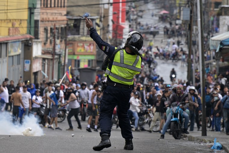 A riot police officer uses tear gas against demonstrators.