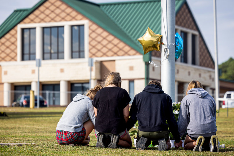 Students kneel in front of a makeshift memorial.