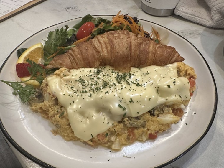 An order of tom yum scramble -- eggs mixed with Dungeness crab, Thai style tom yum sauce, Swiss cheese, onion, mushrooms, tomato with a croissant -- sits on a counter at Taste & Glory restaurant in San Mateo, Calif, on Saturday, Aug. 17, 2024. 