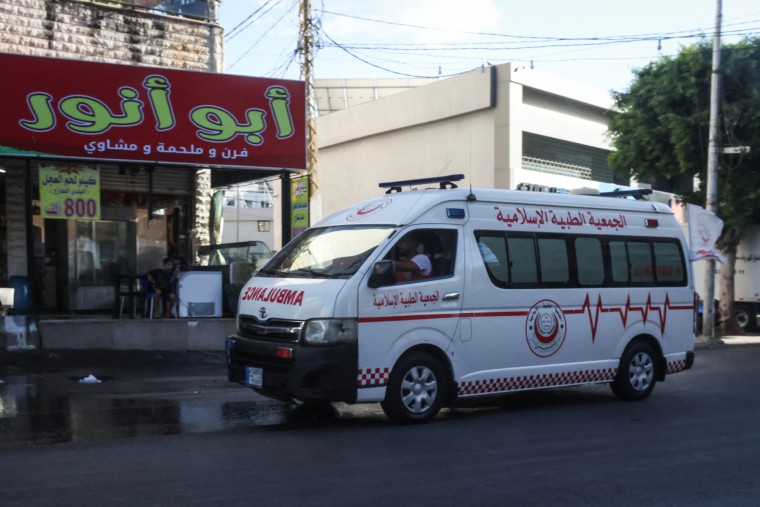 An ambulance vehicle drives on the street past buildings