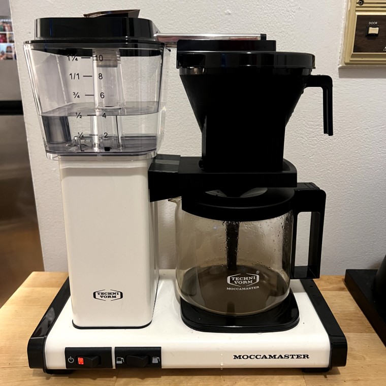 White Moccamaster coffee maker on a wooden table with freshly brewed coffee in carafe