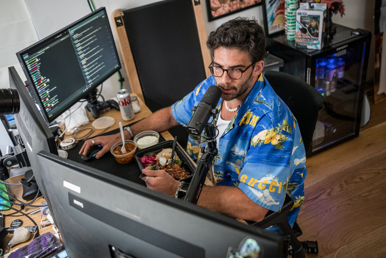 Hasan Pikar is eating at his computer station and talking into a microphone.