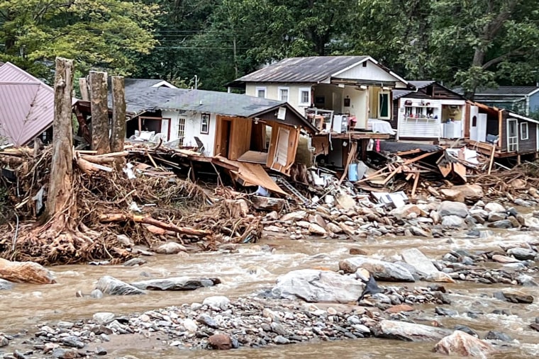 Damaged homes and fallen trees on a street lined with debris