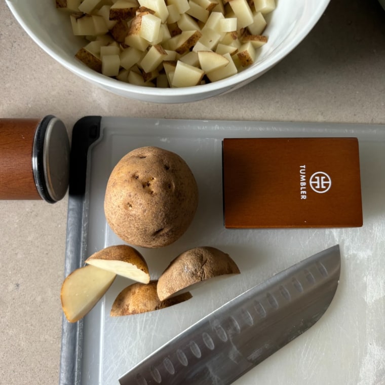 Tumbler knife sharpener on a cutting board and a bowl with diced potatoes.