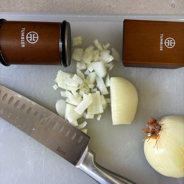 Diced onion on a cutting board next to a chef’s knife and the Tumbler knife sharpener.