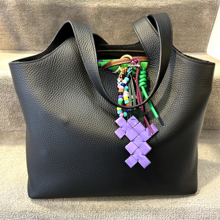 Black leather Cuyana tote bag with a purple bag charm hanging on it.