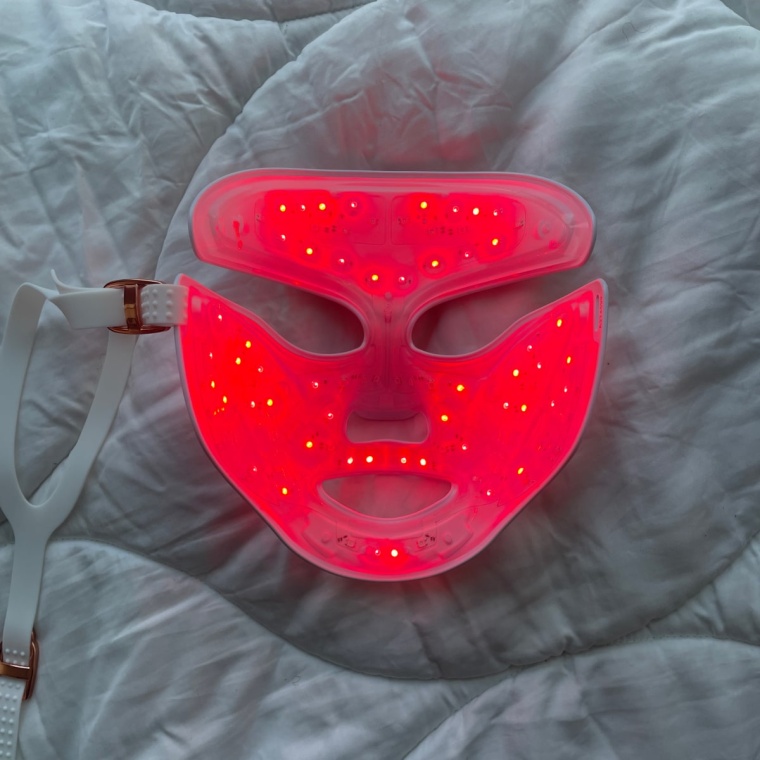 Three images of the DRx Spectralite Faceware Pro facedown on a white comforter with the first photo showing the red LED lights, the second photo showing the blue LED lights, and the third photo showing the combined red and blue LED light setting.