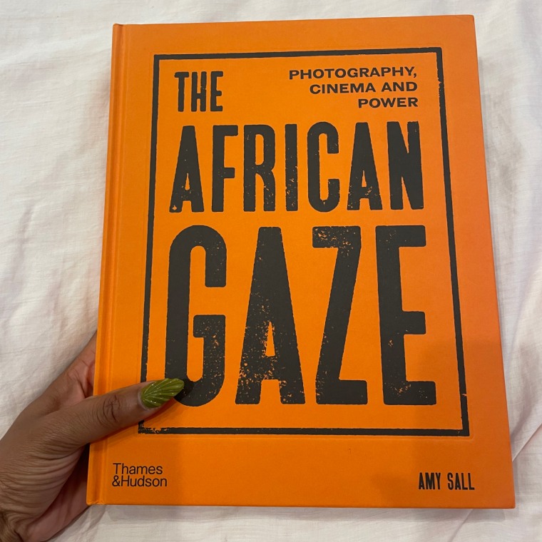 A hand holding The African Gaze: Photography Cinema and Power against a light pink duvet cover.