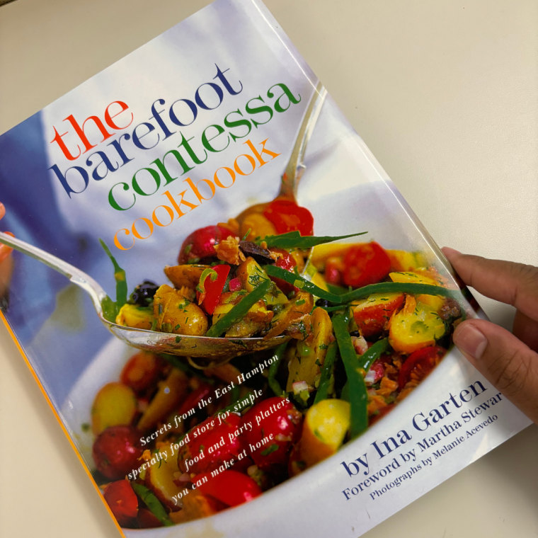 The Barefoot Contessa Cookbook on a table with a hand on it.