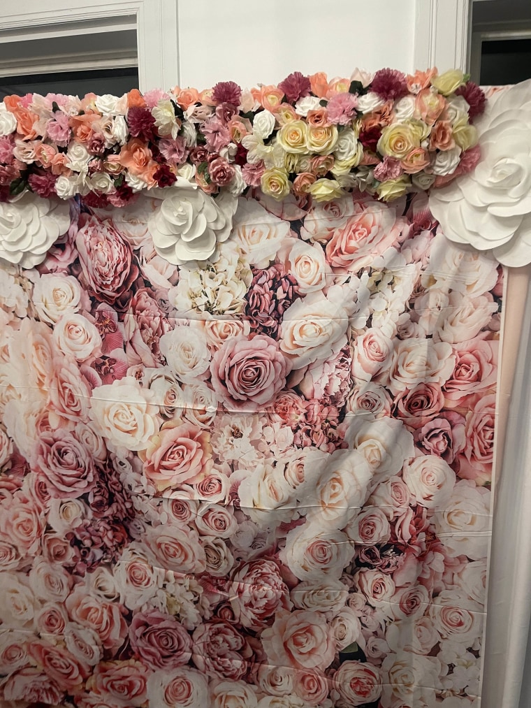 A pink floral photo backdrop with wrinkles in it and a fake flower garland.